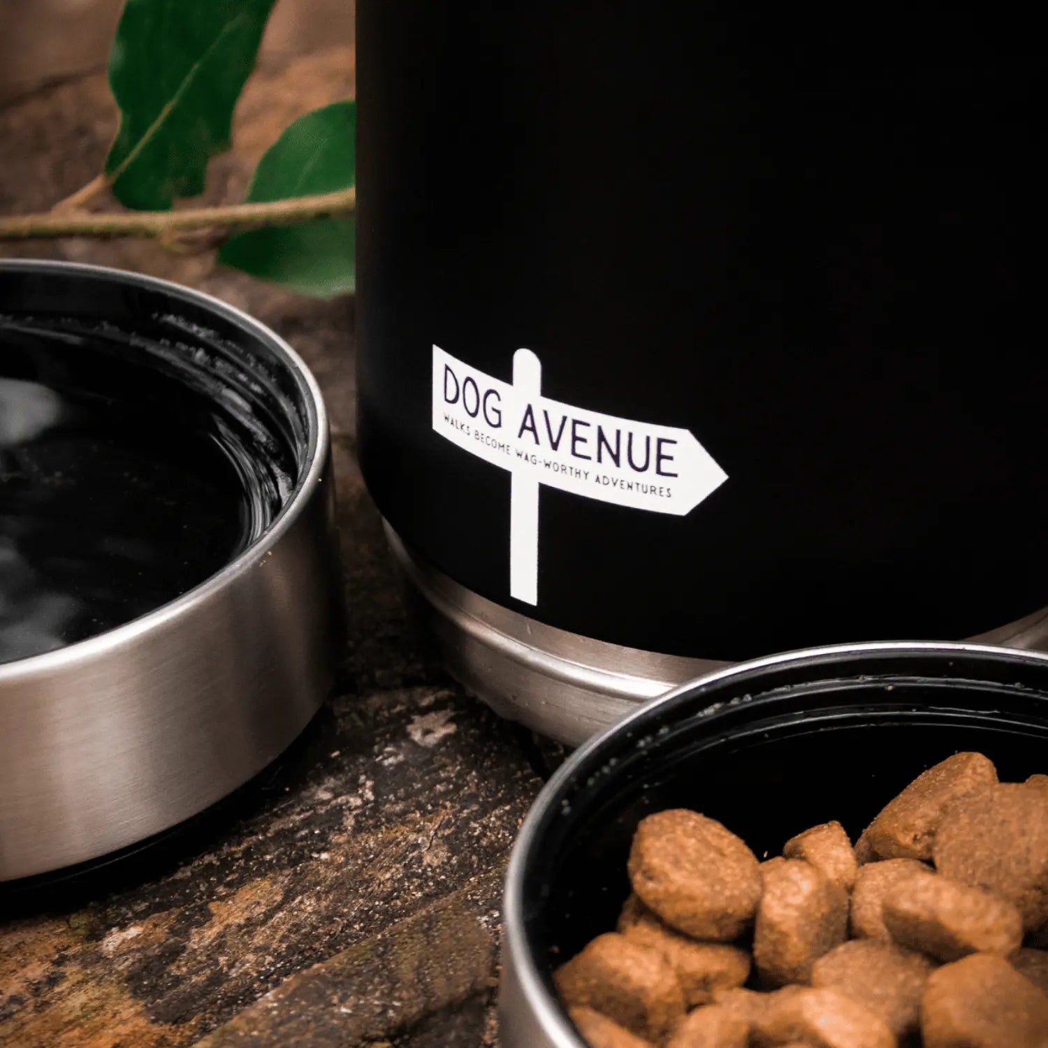 Close-up of the Dog Avenue signpost logo on the matte black bottle, with an empty bowl and a bowl of kibble